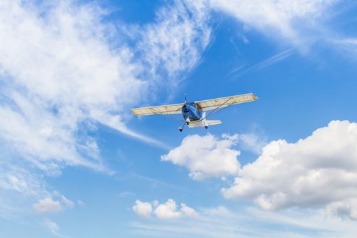 A single engine ultralight plane flying in the blue sky with white clouds