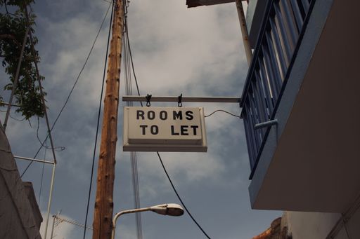 A low-angle shot of a sign that says "ROOMS TO LET" hanging from a pole