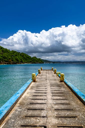 A vertical shot of a pier leading into the sea in San Juan, Puerto Rico under a bright cloudy sky