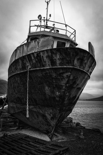 A vertical shot of an old rusty ship on the shore near the water under a cloudy sky in black and white