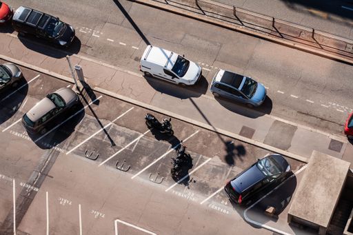 A rooftop view of cars and motorbikes parked in a parking lot and along the street