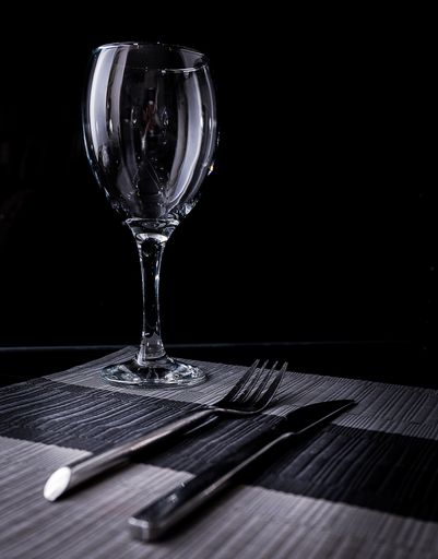 A vertical gray scale shot of a glass and a fork and a knife with a black background