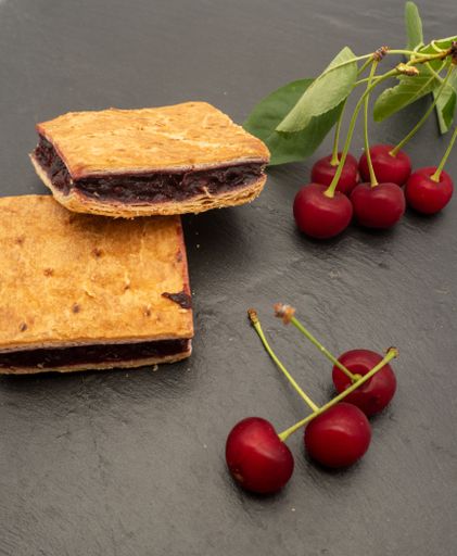 A set of cookies with sour cherries with their leaves against a gray surface
