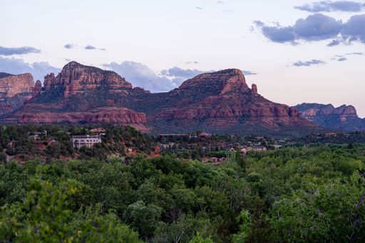 A scenic view of Sedona mountains and cliff formations during a summer sunset with green trees and houses around