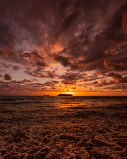 An aerial view of parachute flying over sea during sunset in Manuel Antonio beach