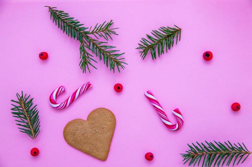 A flat lay shot of candy canes, fir branches, Christmas berries and a heart cookie on a pink surface