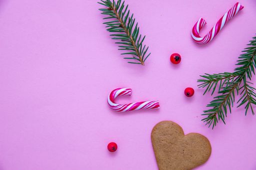 A flat lay shot of candy canes, fir branches, Christmas berries and a heart cookie on a pink surface