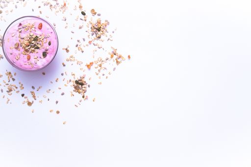 A flat lay shot of a bowl of berry yogurt with grains and fruit chunks on it on a white surface