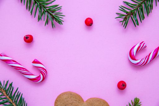 A flat lay shot of candy canes, fir branches, Christmas berries and a heart cookie on a pink surface
