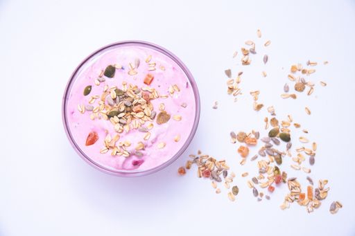 A bowl of tasty berry yogurt with grains and fruit chunks on it on a white surface