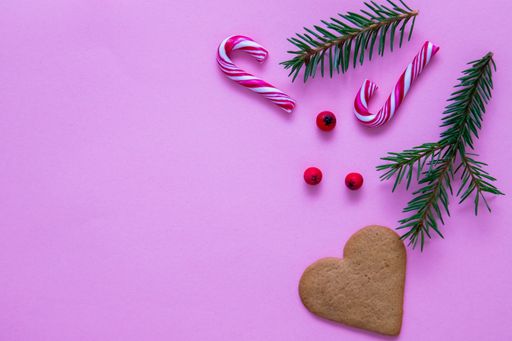 A flat lay shot of candy canes, fir branches, Christmas berries and a heart cookie on a pink surface
