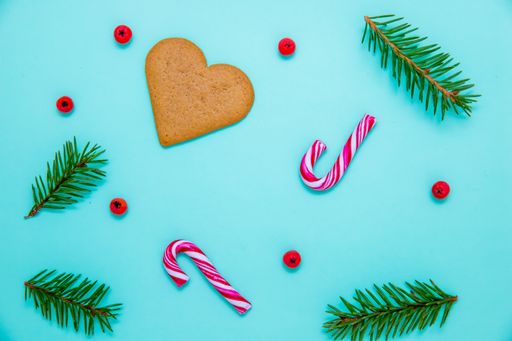 A flat lay shot of fir branches, candy canes, Christmas berries and a heart cookie on a blue surface