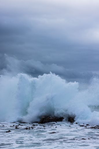 A vertical shot of a sea wave crashing on the rocks during a cloudy day