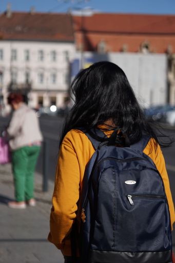 A vertical closeup shot of a girl wearing a yellow shirt with a backpack while roaming the streets in Romania
