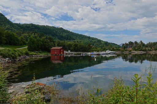 A beautiful view of a hut and boats on the shore of a lake surrounded by dense forests