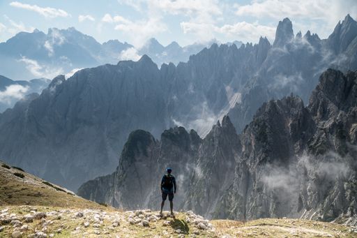 A beautiful shot of person standing on a rock looking at Three Peaks Nature Park in Toblach, Italy