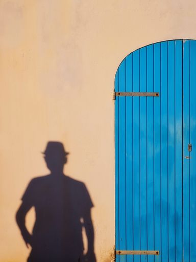 The shadow of a man reflected on a wall of a house with a blue wooden door