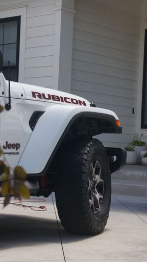 A White Jeep Rubicon in front of a house from the side, close-up, vertical