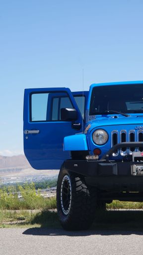 A Blue Jeep Wrangler on a grassy hill with mountains in the background