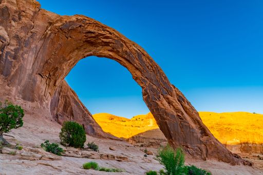 The Corona Arch in Utah, USA with mountains and a blue sky in the background.