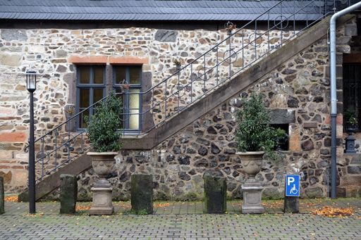An old stone house with a metal staircase and with plants in clay pots in front of it