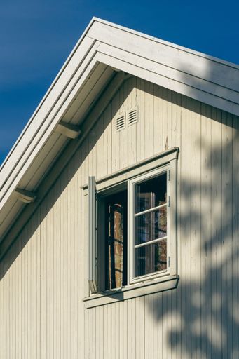 A vertical shot of a white wooden house with an open window in the morning light