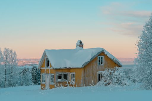 A beautiful old wooden house covered in snow next to snowy trees during winter against a blue sky