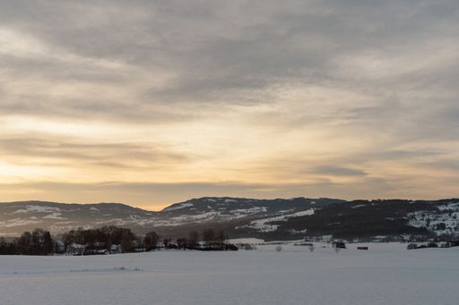 A beautiful landscape of a field covered in snow and mountains in the background against a sunset sky