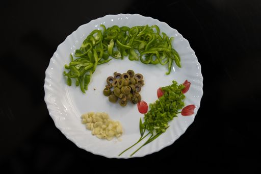 A closeup shot of chopped peppers and olives, airy cheese and herbs on a plate on black background