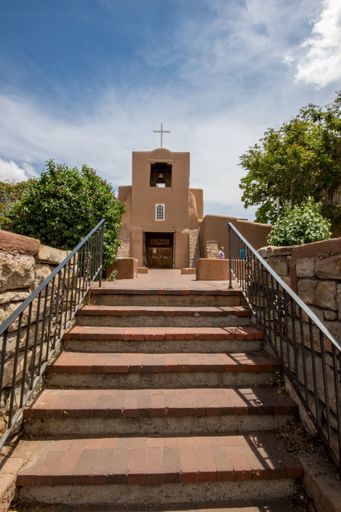 The San Miguel Chapel in Santa Fe, New Mexico with brown steps leading to it under a sunny blue sky