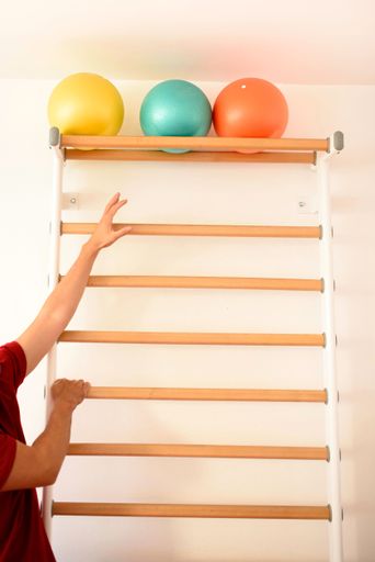 A vertical shot of a person reaching for the balls on the top shelf of the wooden stairs for gymnastic