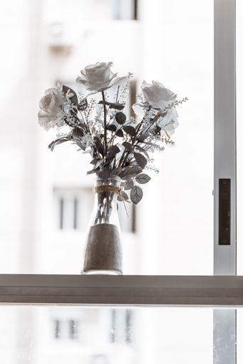 A vertical shot of roses arranged in a bottle vase against a bright window