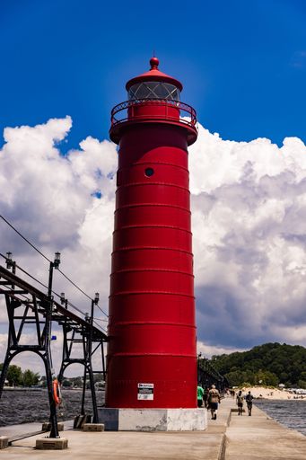 A red lighthouse by the beach with a cloudy blue sky background