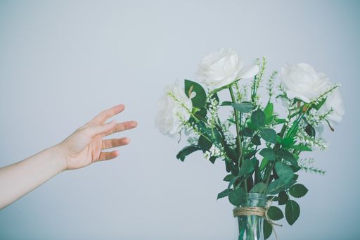 A person reaching for the beautifully arranged bouquet of flowers  against a white wall
