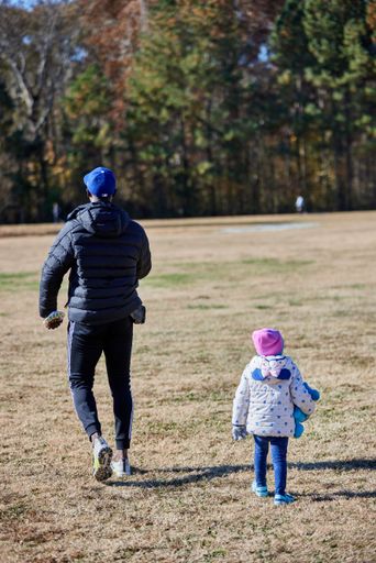 A vertical shot of a father with the daughter walking in the park - shot from back