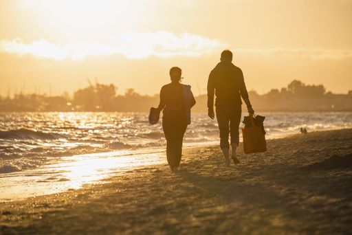 A man and a woman walking on the sandy Alameda beach, California, at sunset