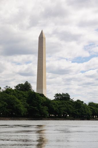 A vertical shot of Washington Monument with trees and river under cloudy sky, USA