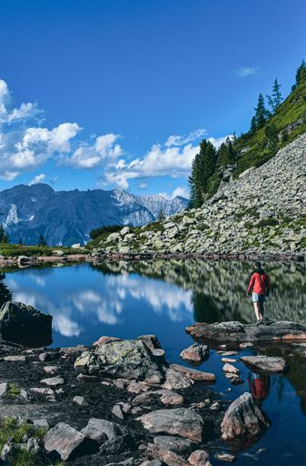 A beautiful shot of a man standing near the lake surrounded by mountains