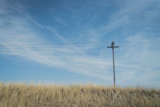A low angle shot of electric pole supporting power lines in the brown field against blue cloudy sky