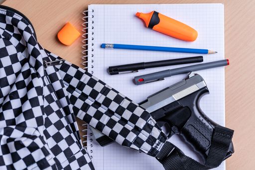 A closeup top view of school supplies and a gun on a wooden table - gun regulation concept