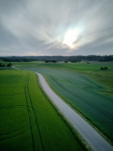 An aerial view of highway through lush green fields against cloudy sky