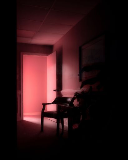 A vertical shot of a dark room interior with pink lighting coming from the open door