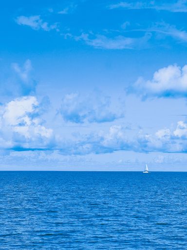 A vertical shot of a white boat sailing on blue water under a bright blue sky
