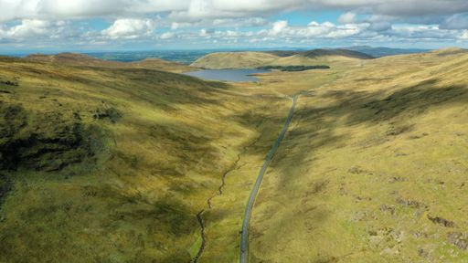 An aerial view of an asphalt road through green hills and valleys in Northern Ireland