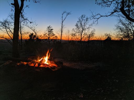 A beautiful shot of a campfire in the woods with the golden sun setting on the horizon