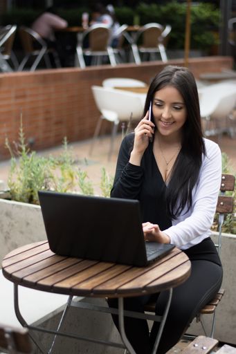 A vertical shot of a woman speaking on the phone and working on her laptop in a cafe