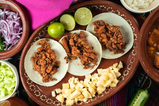 A top view of tasty tortillas with meat next to raw potato cubes and sliced lime