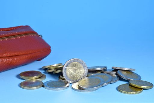 A closeup of euro coins scattered on blue background with a red wallet and a copy space