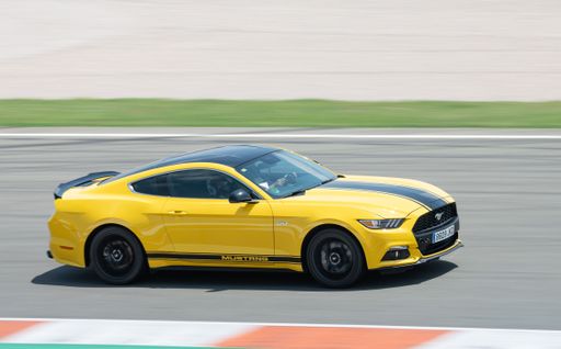 A stunning yellow Ford Mustang with a black strip racing around a competition track