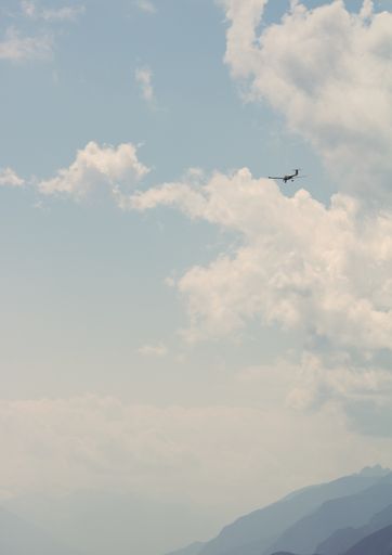 A vertical shot of a light aircraft flying into the sky over the silhouettes of mountains